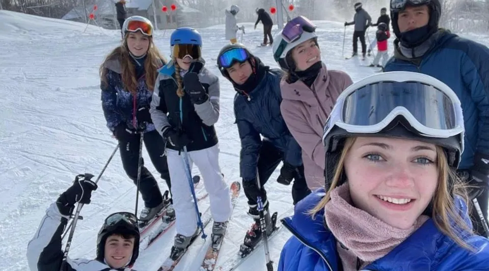 Studenti della Andrews Osborne Academy in tenuta da sci su una pista innevata con impianti di risalita sullo sfondo.
