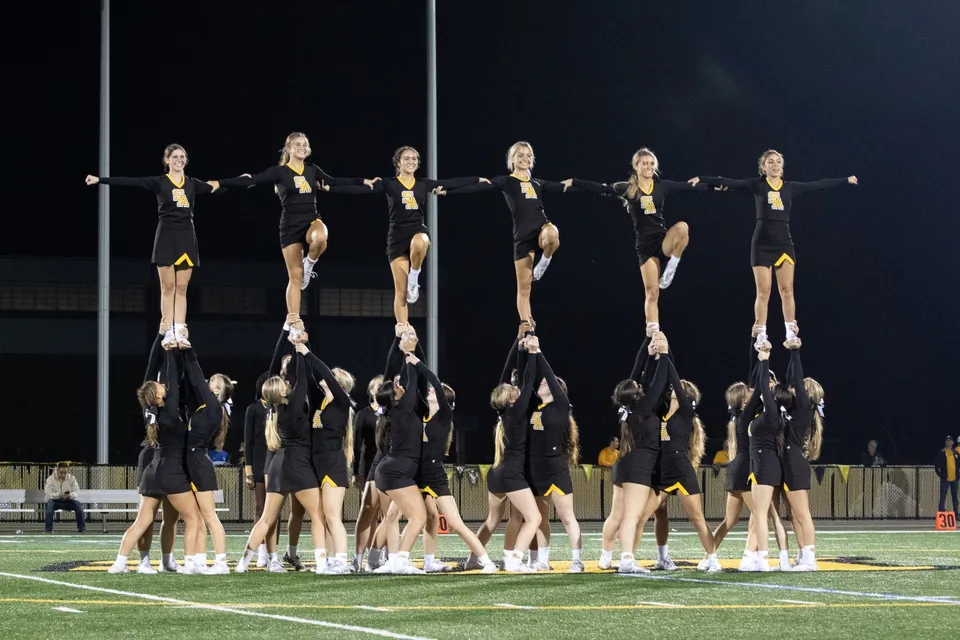 Un gruppo di cheerleader esegue una routine sincronizzata sul campo sportivo della Saint Anthony's High School di notte.