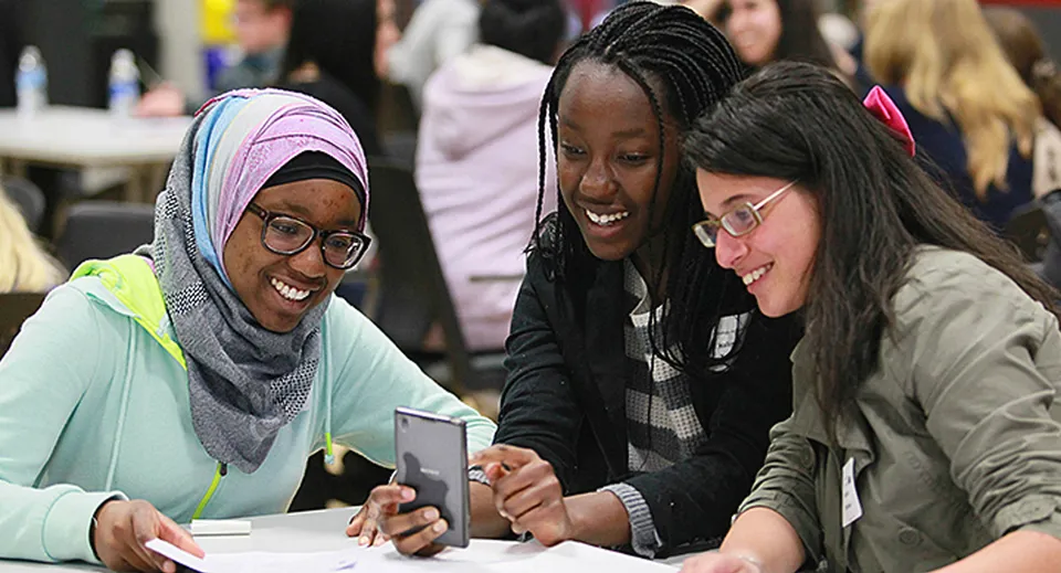 Tre studentesse della Forest Lawn High School guardano insieme uno smartphone in classe.