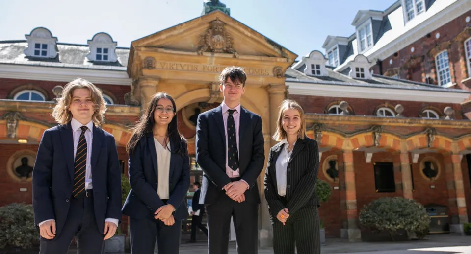 Un gruppo di quattro studenti e studentesse si trova davanti a un edificio storico nel campus della Wellington School.