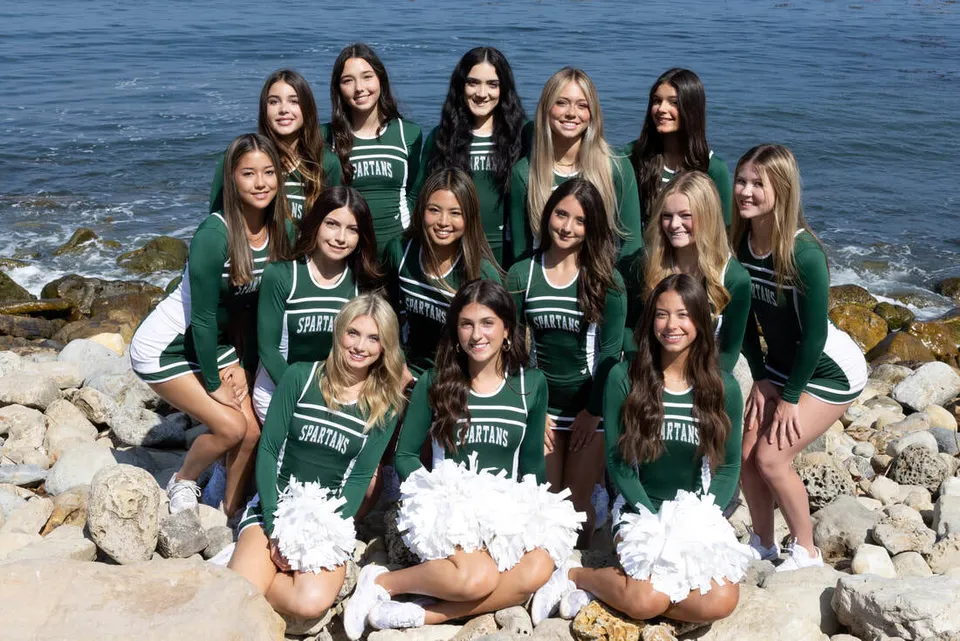 Un gruppo di cheerleader della Torrance South High School posa insieme su una costa rocciosa con l'oceano sullo sfondo.
