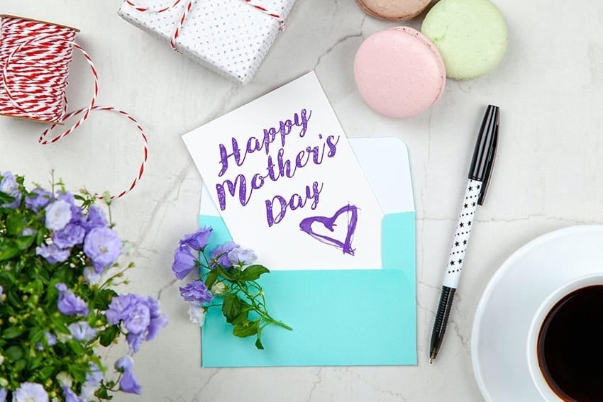 Tarjeta con el texto Happy Mother's Day junto a un bolígrafo, café y flores