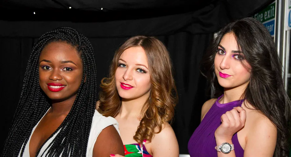 Tre studentesse di diversa origine posano insieme davanti a uno sfondo scuro all'Oxford International College.