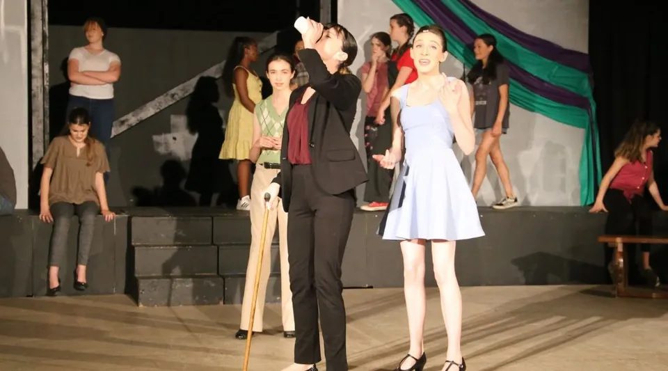 Un gruppo di studenti e studentesse della New Garden Friends School in abiti formali si trova su un palco davanti a un sipario.