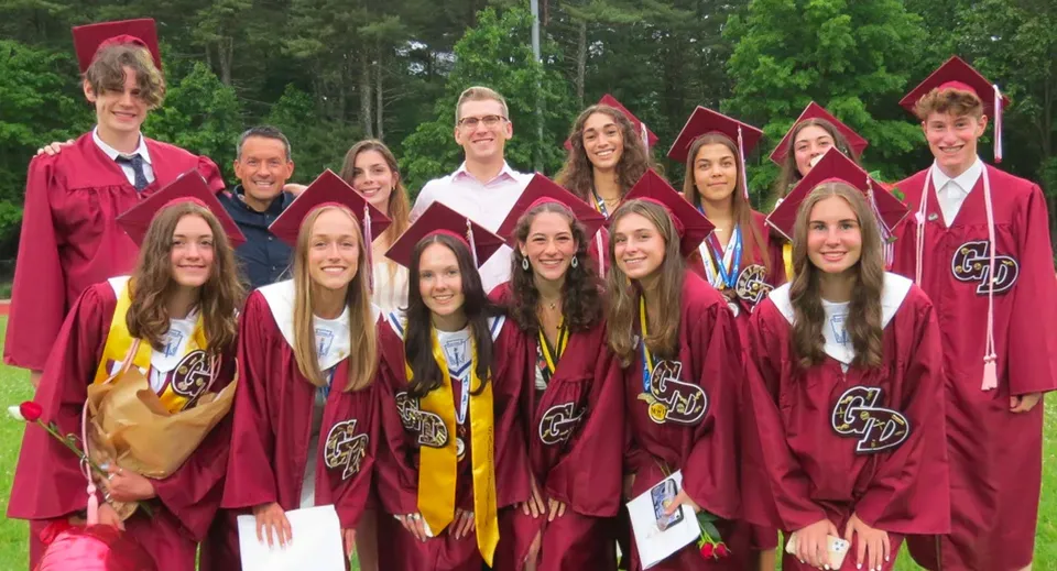 Un gruppo di diplomati della Groton-Dunstable Regional High School posa all'aperto in toga e tocco di colore granata.