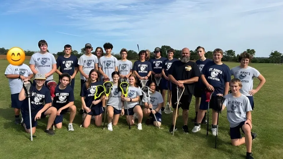 Un gruppo di studenti della St. Anne's Catholic School posa insieme su un campo sportivo sotto un cielo azzurro.