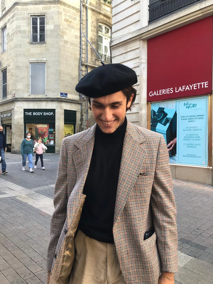 Studente con basco e giacca sorride in una via del centro in Francia, davanti alle Galeries Lafayette