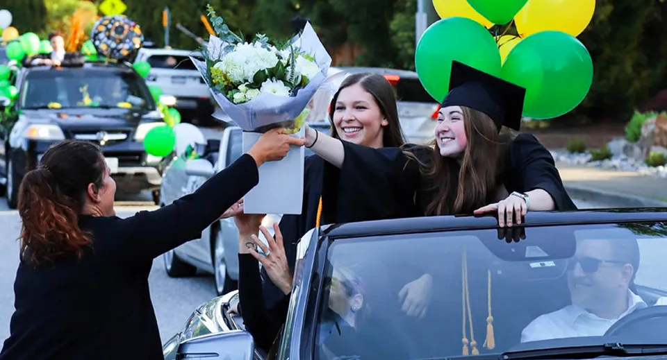 Studentesse della Windsor Secondary School con il tocco e la toga da diploma tengono dei fiori durante la cerimonia di diploma.