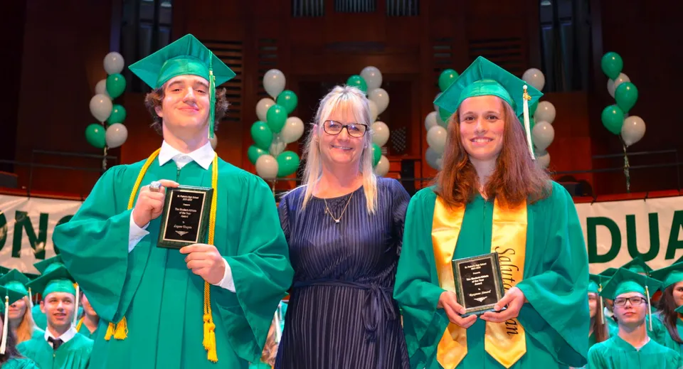 Tre studenti della St. Patrick’s High School di Québec City in abito da diploma con diploma davanti a una parete di palloncini verdi e gialli.