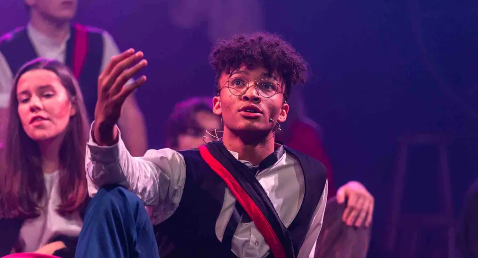 Uno studente della Taunton School International sta su un palco e gesticola in modo espressivo durante una rappresentazione.