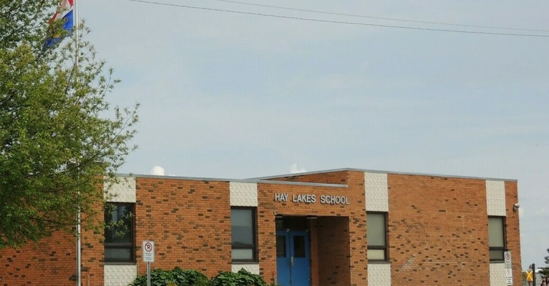 L'edificio in mattoni della Hay Lakes School è circondato da alberi e si staglia contro un cielo limpido.
