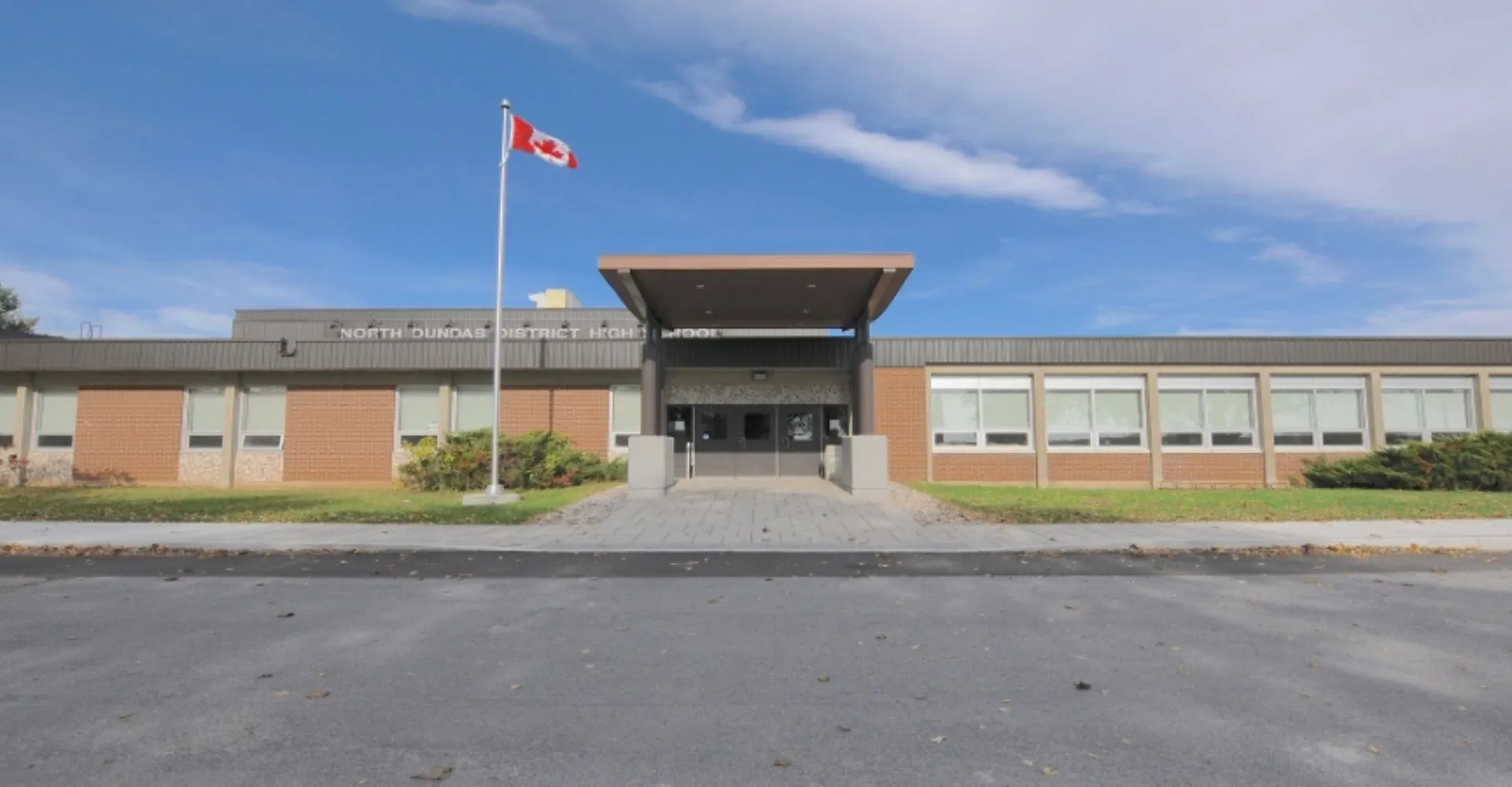 L'edificio moderno a più piani della North Dundas District High School con la bandiera canadese sul tetto sotto un cielo blu.