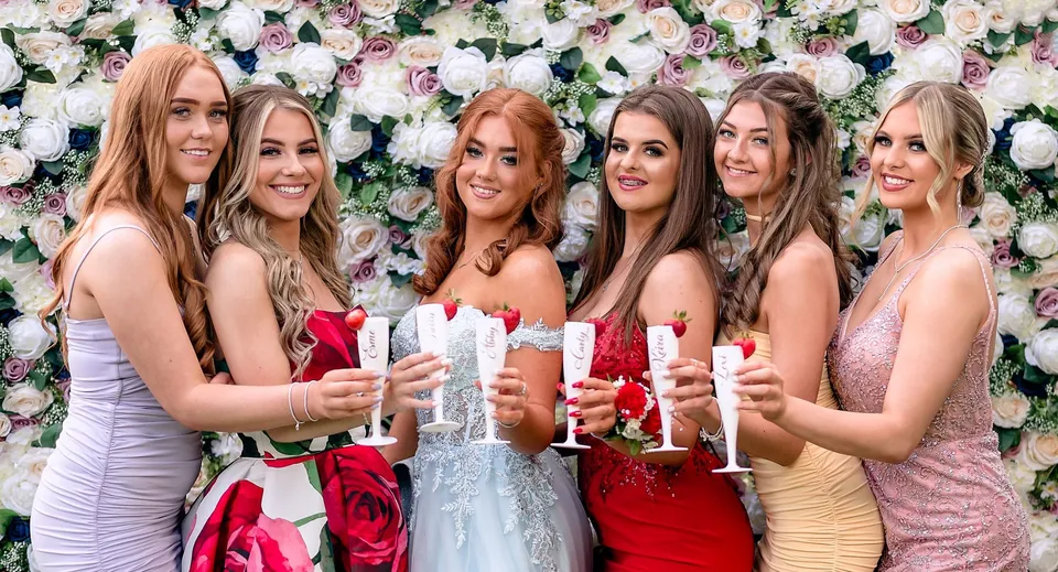 Un gruppo di giovani studentesse della Manor House School festeggia insieme davanti a uno sfondo floreale con calici di spumante.