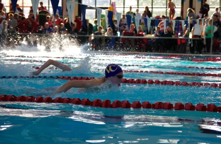 Una nadadora con gorro de natación azul y gafas de natación en una competición en la piscina del Vancouver Community College.