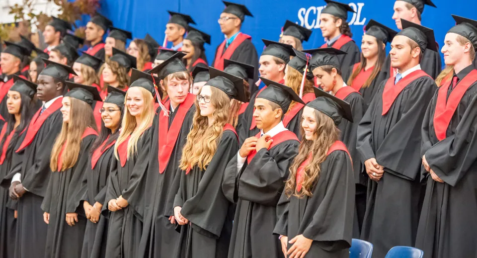 Un grande gruppo di diplomati della West Carleton Secondary School in toga nera e stola rossa davanti a uno sfondo blu con il logo della scuola.