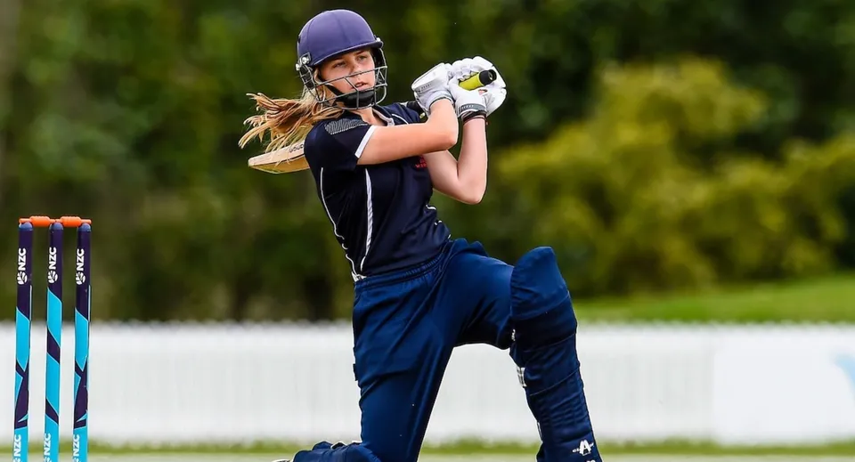 Una giocatrice di cricket del Highlands Christian College in maglia blu con la mazza pronta sul campo.