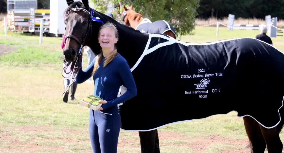 Una studentessa del St. Cuan’s College si trova su un prato accanto a un grande cavallo nero.