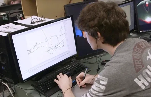 Joven con auriculares dibujando en una tableta gráfica conectada al ordenador de un aula