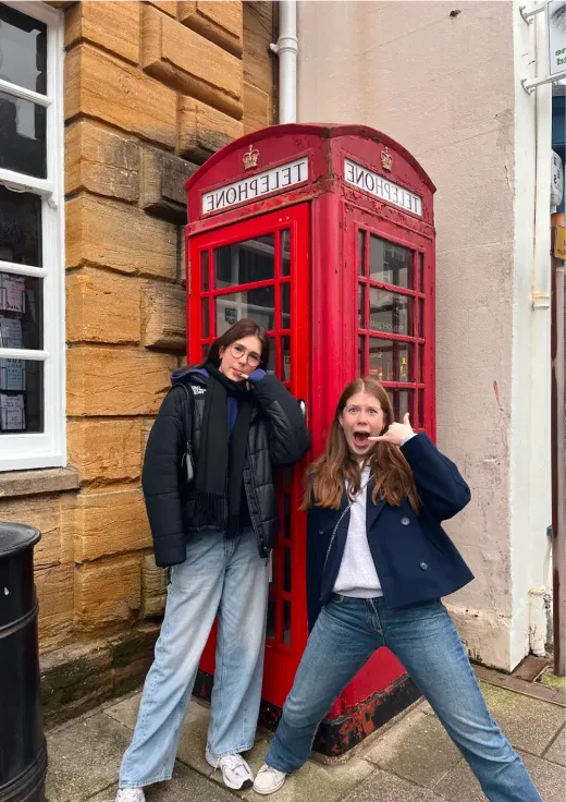 Zwei Mädchen albern vor einer roten Telefonzelle in England herum