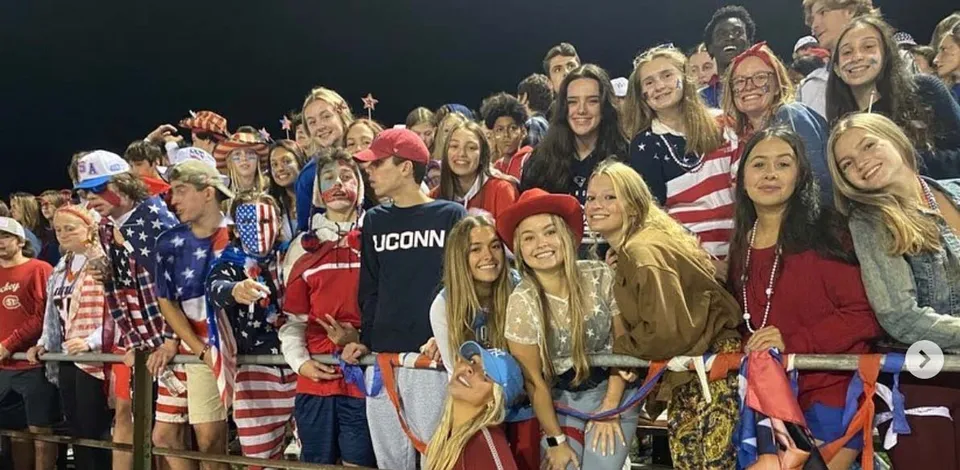 Un gruppo di studentesse e studenti della Maynard High School in abiti patriottici posa insieme sorridendo per una foto di gruppo.