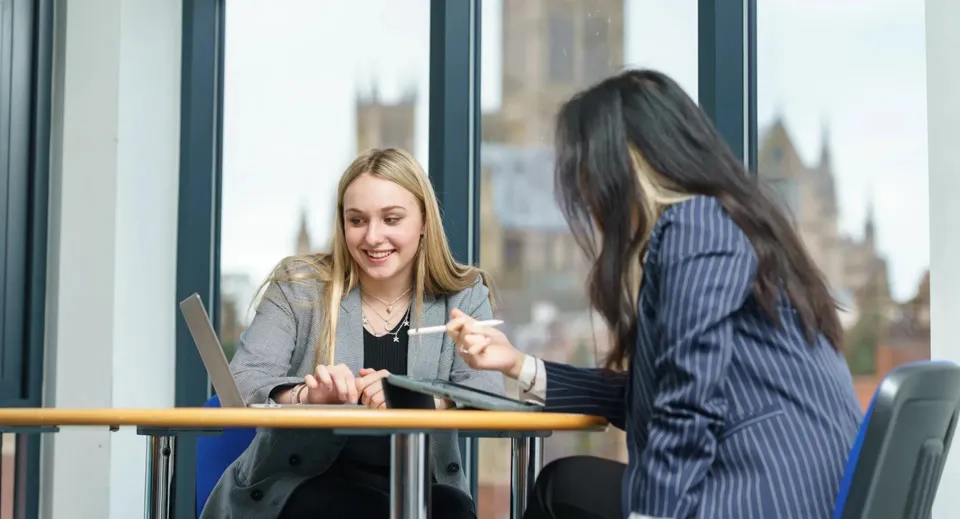 Due donne conversano davanti a una finestra con vista sulla città nel campus della Lincoln Minster School.