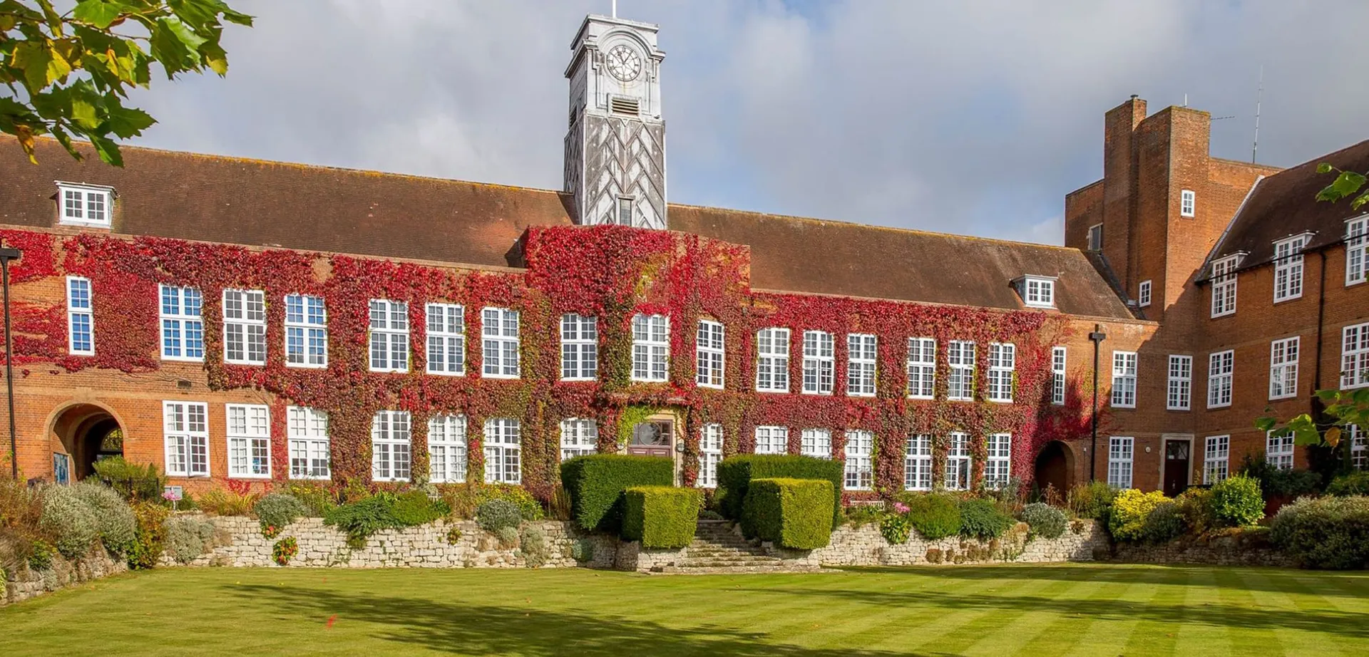 L'edificio in mattoni con un'alta torre dell'orologio nel campus della Sutton Valence School è circondato da un prato curato e alberi.