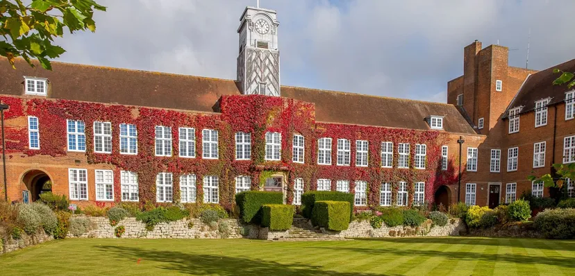 L'edificio in mattoni con un'alta torre dell'orologio nel campus della Sutton Valence School è circondato da un prato curato e alberi.