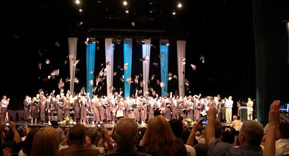 Sul palco della Walnut Grove Secondary School si esibiscono numerosi studenti in toghe bianche.