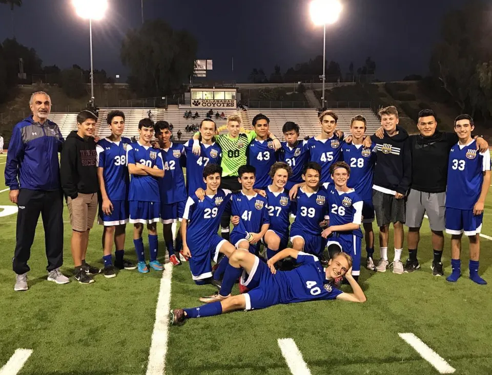 Un gruppo di studenti della Calabasas High School posa insieme di notte su un campo da football con tabellone segnapunti e illuminazione da stadio.