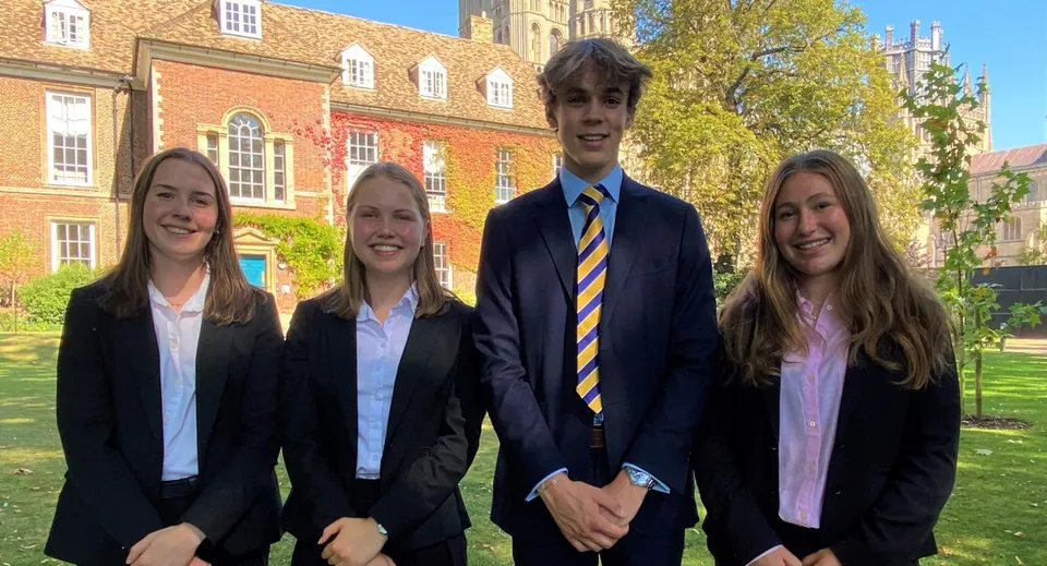 Quattro studenti e studentesse sono insieme davanti a un edificio storico in mattoni nel campus di King's Ely.