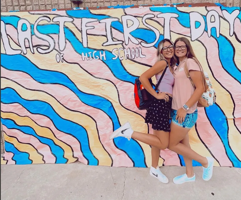 Due studentesse posano davanti a un murale colorato con la scritta High School alla Esperanza High School.