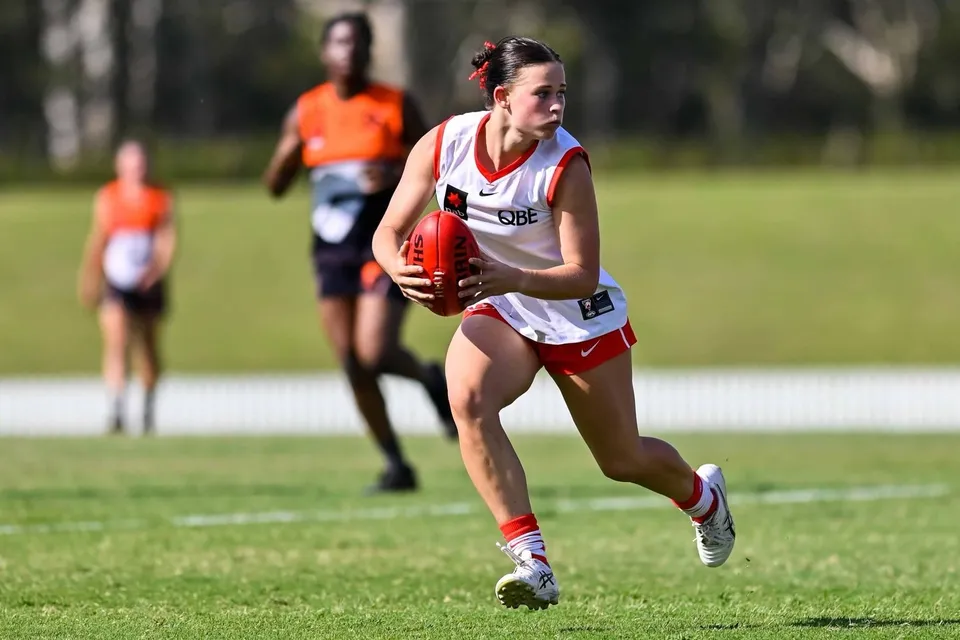 Un'atleta in divisa sportiva bianco-rossa corre sul campo sportivo della Lambton High School.