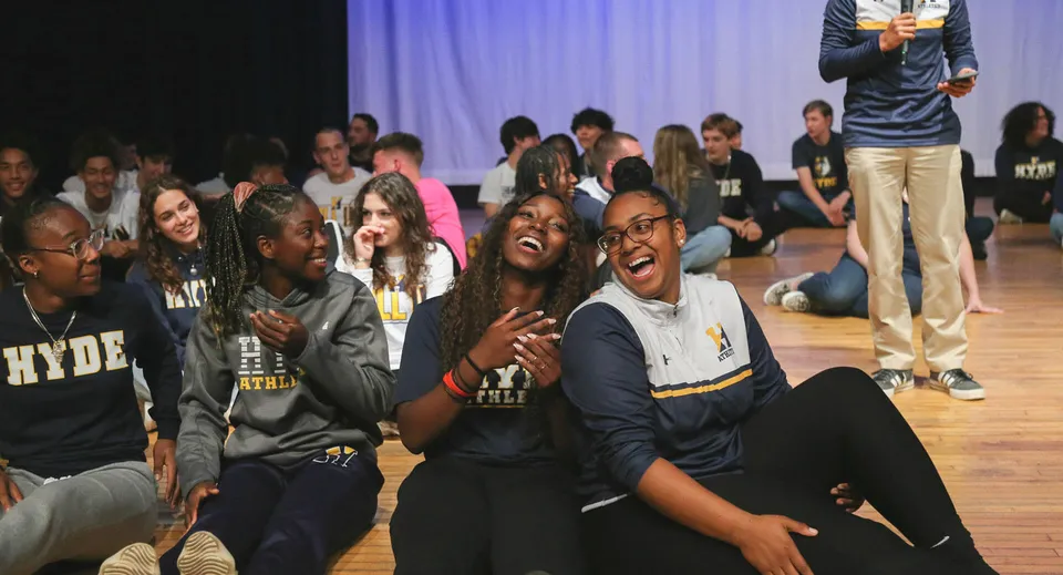 Un gruppo di studenti della Hyde School seduti e in piedi in una stanza poco illuminata, mentre chiacchierano.