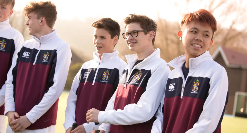 Un gruppo di studenti del Scarborough College si trova all'aperto in divisa scolastica con camicie bianche e maglioni color Borgogna.
