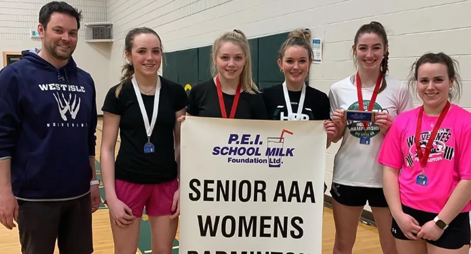 Un gruppo di studenti della Westisle Composite High School tiene uno striscione per il Senior AAA Womens Event della P.E.I. School Milk Foundation in una palestra.