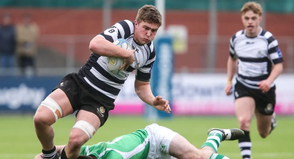 Un giocatore di rugby del Cistercian College corre sul campo con la palla mentre un altro giocatore è a terra.