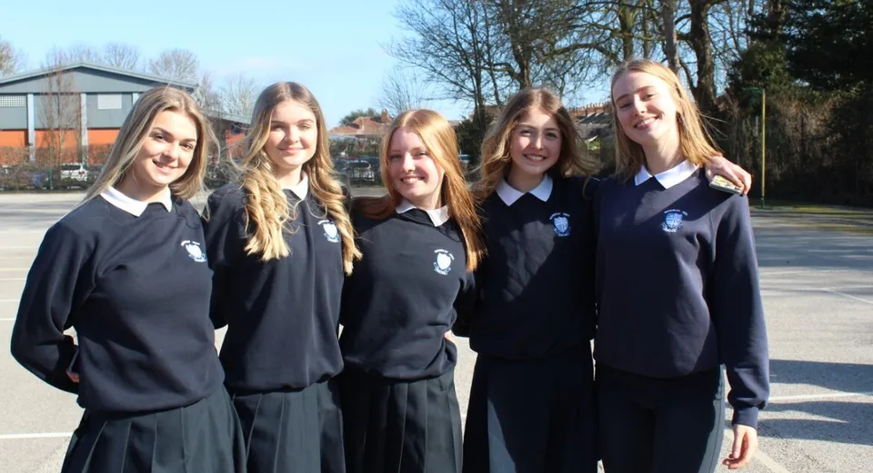 Un gruppo di cinque studentesse in uniforme scolastica si trova davanti a un edificio nel campus della Beverly High School.