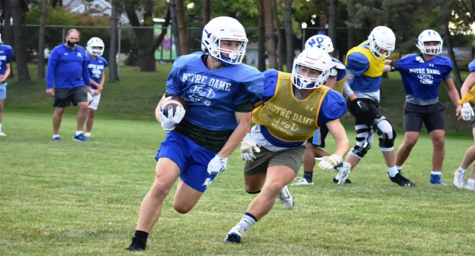 Un gruppo di giocatori di calcio della Academy of Notre Dame si allena su un campo con alberi e edifici sullo sfondo.