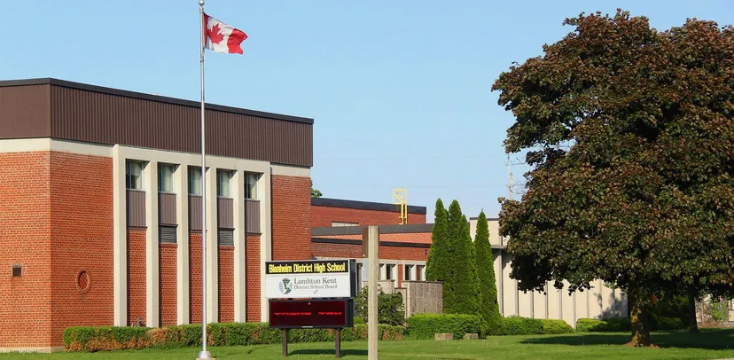 L'edificio in mattoni della Blenheim District High School, con una bandiera canadese sul tetto, è circondato da alberi.