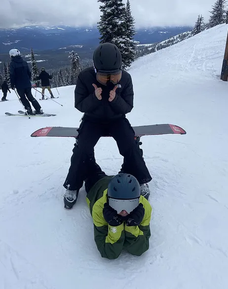 Dos jóvenes con casco haciendo el tonto en una pista de esquí nevada rodeada de montañas