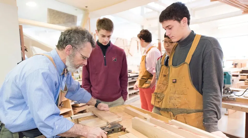 Un gruppo di studenti e un uomo più anziano lavorano insieme a un tavolo da lavoro nel campus della The Salisbury School.