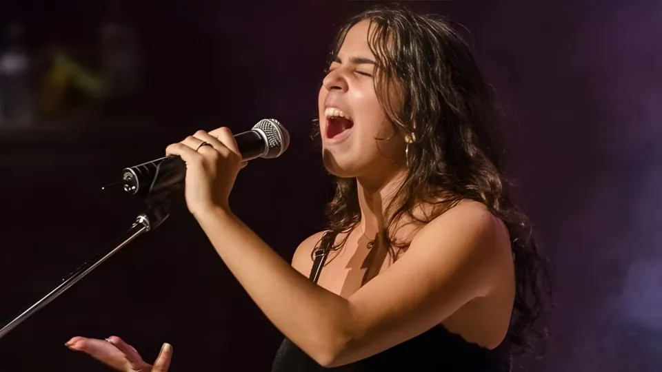 Una studentessa della École Secondaire Augustin-Norbert-Morin canta con passione in un microfono su un palco.