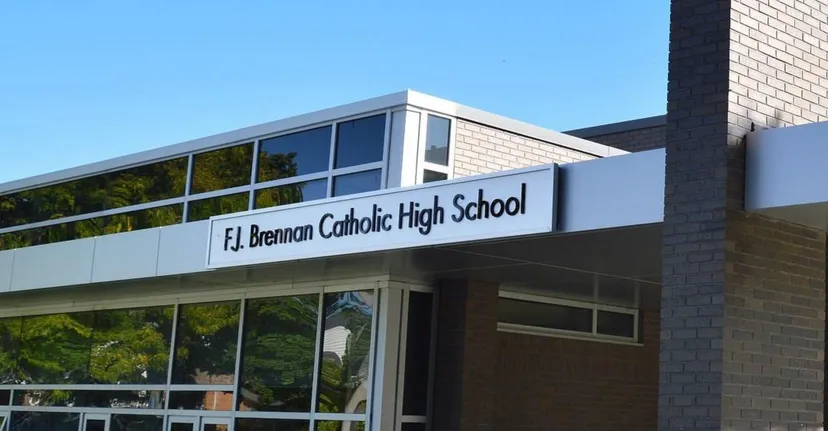 L'edificio della FJ Brennan Catholic High School con una moderna facciata in vetro, circondato da alberi e un'area verde.