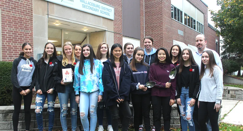 Un gruppo di studenti e studentesse si trova davanti all'edificio in mattoni della Wallaceburg District High School.