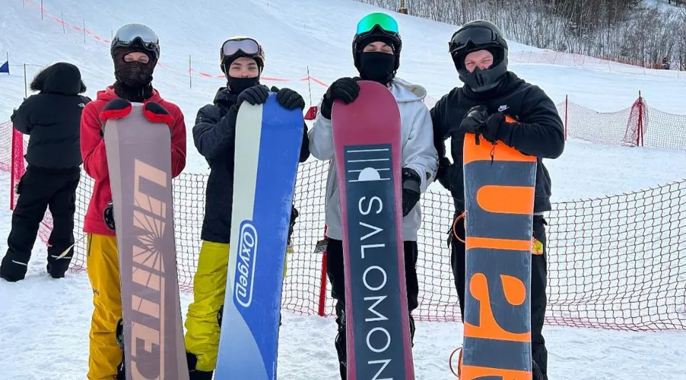 Un gruppo di studenti e studentesse della St. Benedict Catholic Secondary School indossa abiti da sci colorati e si trova davanti a una pista innevata.
