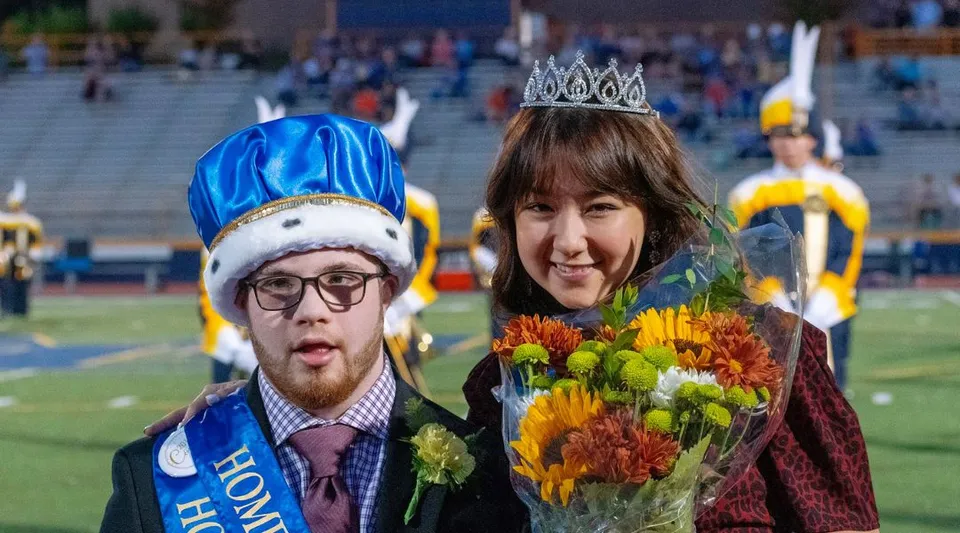 Un uomo con un cappello blu e una donna con una corona tengono dei fiori durante un evento del Mt. Lebanon School District.