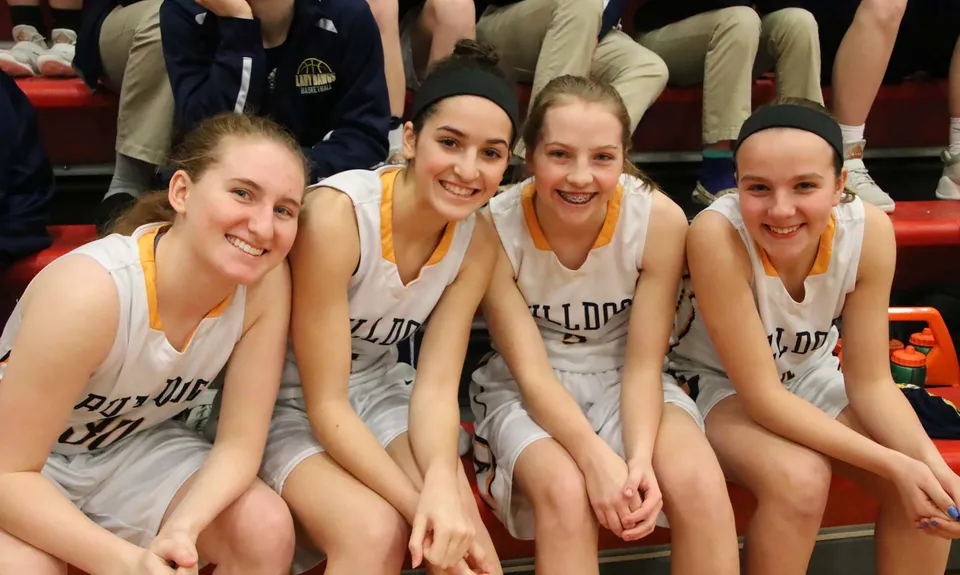 Quattro studentesse della Aquin High School sono sedute insieme come squadra di basket e sorridono.