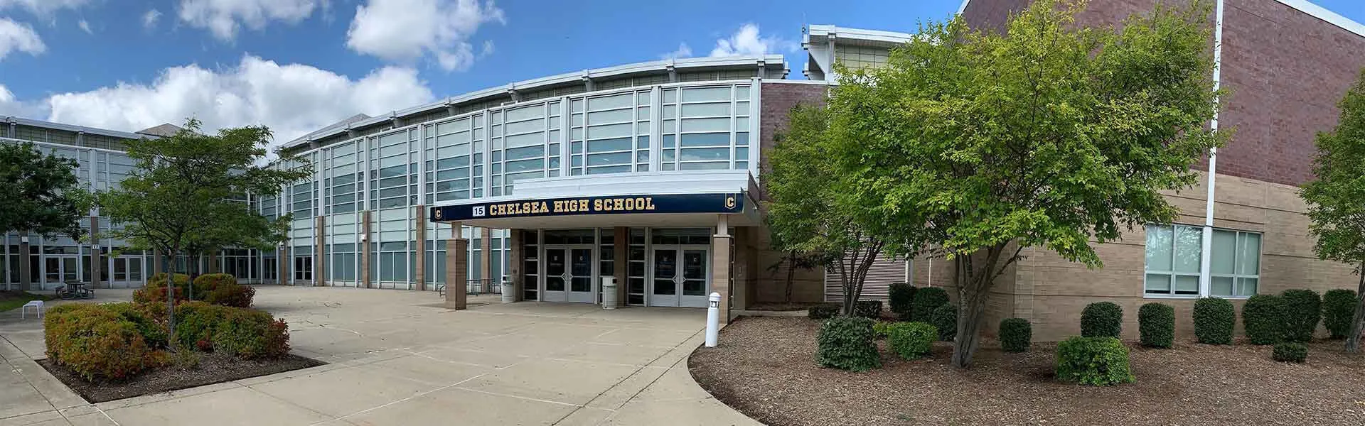 Il moderno edificio scolastico della Chelsea High School con una facciata in vetro, circondato da alberi e aree verdi.