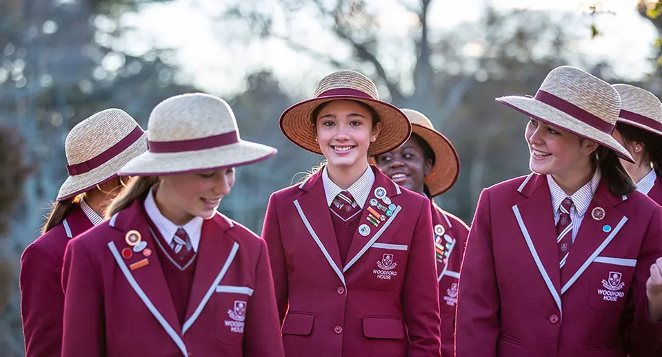Un gruppo di studenti e studentesse di Woodford House si trova all'aperto in divisa rossa con cappelli a tesa larga davanti a uno sfondo di alberi.