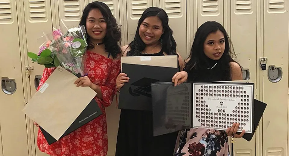 Tre studentesse della Newtonbrook Secondary School sono davanti agli armadietti e tengono in mano dei fiori e un cartellone.
